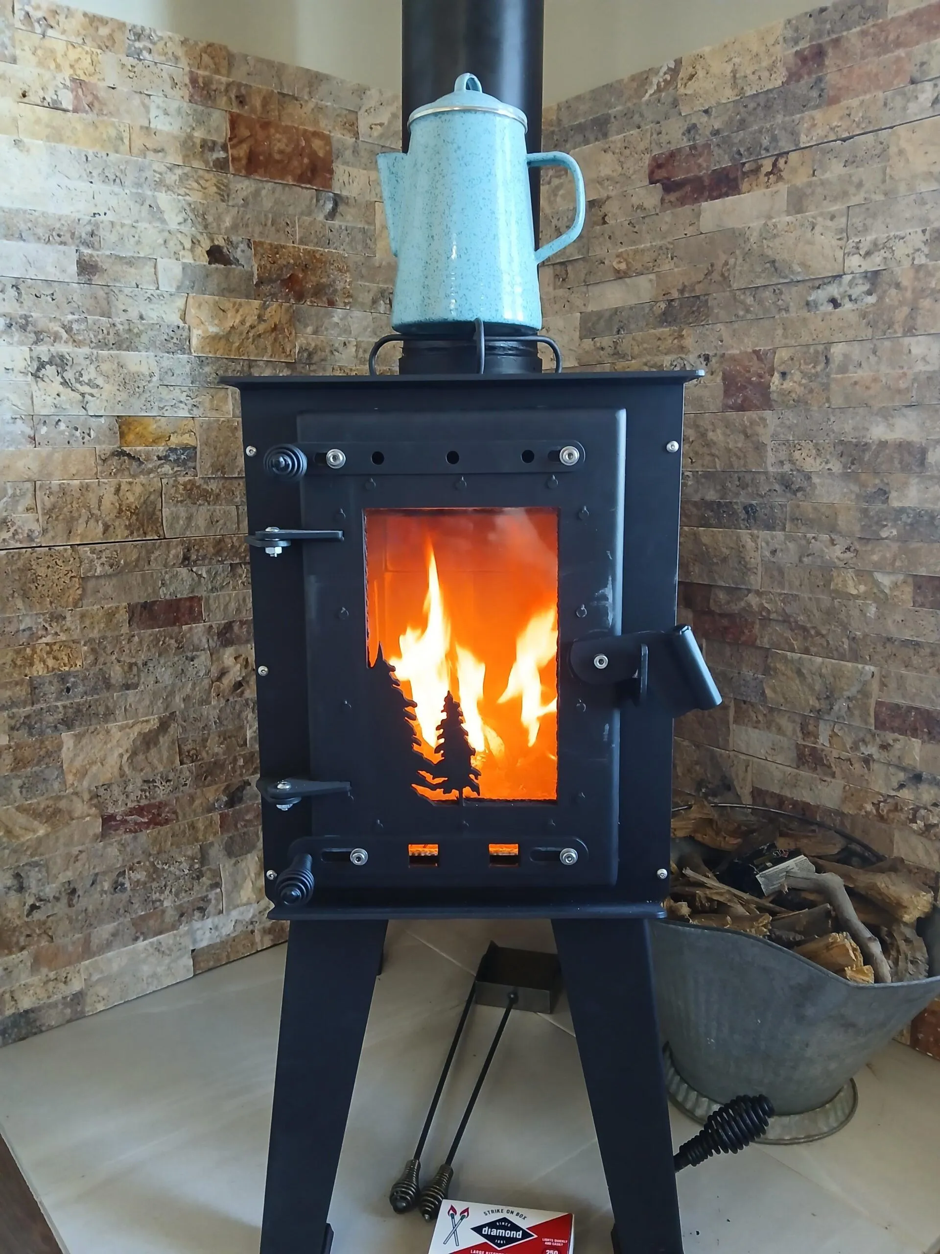 Steelhead small wood stove burning with a kettle on the cooktop